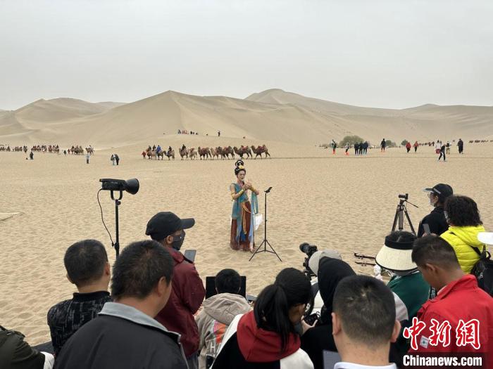 圖為2023年4月底，敦煌大漠“逐舞者”奧楠在鳴沙山月牙泉景區(qū)視頻直播，吸引游人圍觀。　馮志軍 攝
